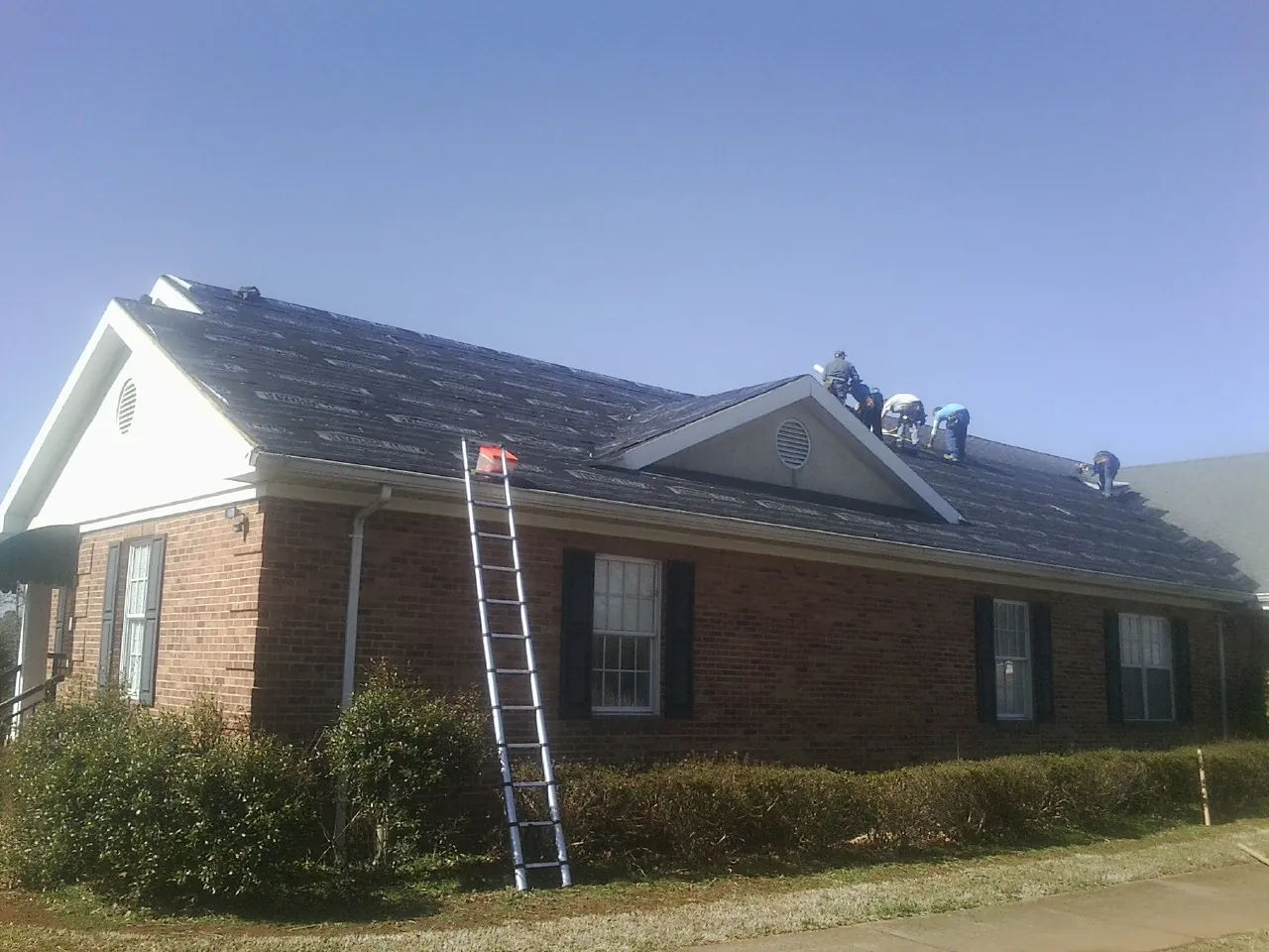 Crew tearing shingles off a brick ranch roof with a ladder set — Metal Roof Repair work by our crew in Grand Island