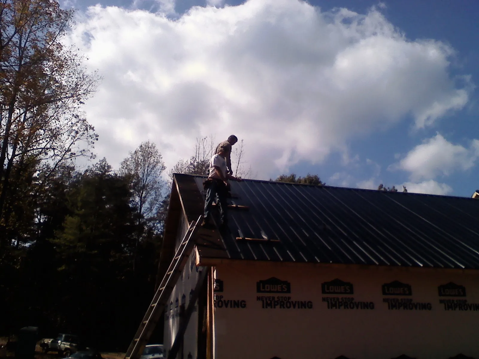 Roofer fastening dark metal panels high against a cloudy sky, from a Roof Inspection job in Grand Island